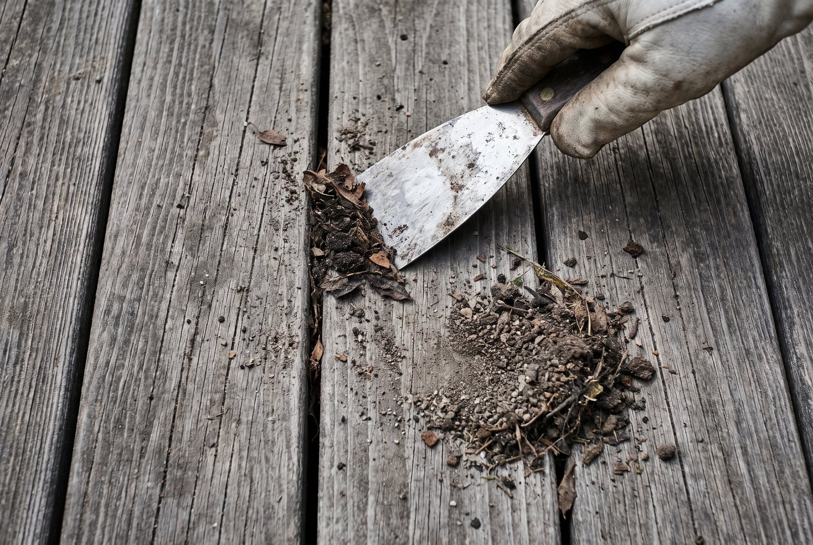 Hand using a putty knife to clear debris from between wood deck boards